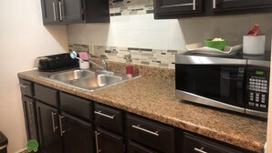 Una cocina con armarios oscuros, encimera de granito, pileta de acero inoxidable, microondas y salpicadero azulejado.