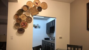 Un comedor con mesa de vidrio, sillas negras y un muro decorado con cestas tejidas.