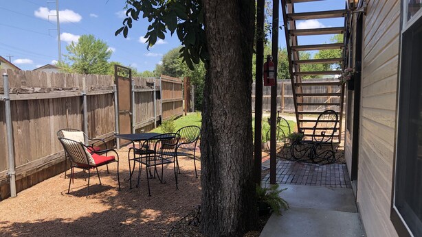 Un patio trasero con terraza, cerca de madera y un árbol.