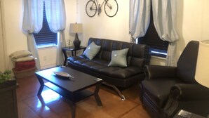 Una sala de estar con un sofá de cuero negro, una mesa de centro, una lámpara y una bicicleta colgada en la pared.