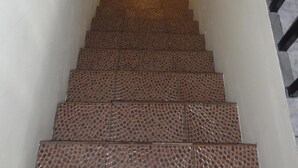 Eine Treppe mit einem gemusterten Fliesenboden führt zu einer Zwischenebene mit einem Holgeländer.