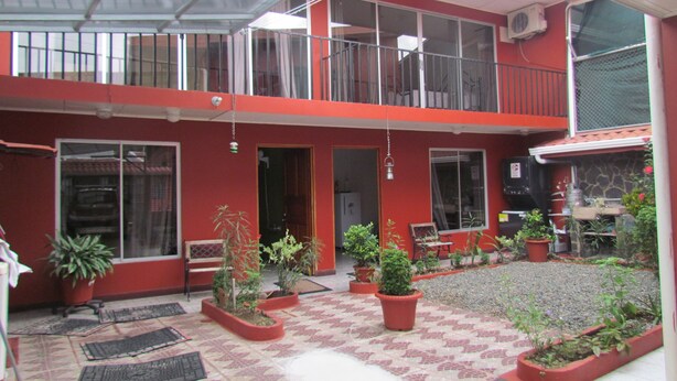 Ein rotes Gebäude mit überdachter Terrasse, Blumentöpfen und Außenbestuhlung.