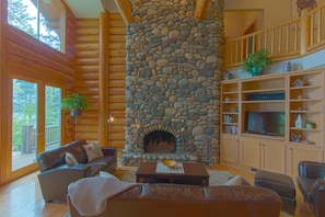 Ein Holzblockhaus-Interieur mit Kamin aus Stein, Holzmöbeln und einem Bücherregal.