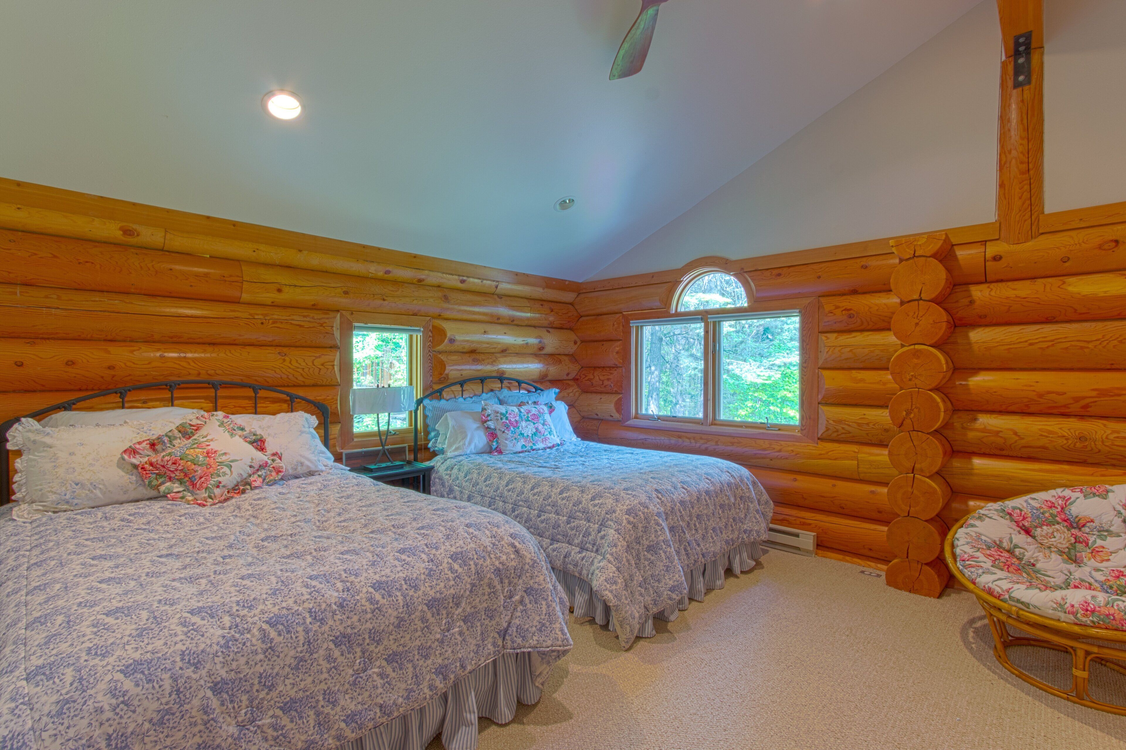 Une chambre aménagée dans un chalet en rondins, avec deux lits, une fenêtre et une chaise.