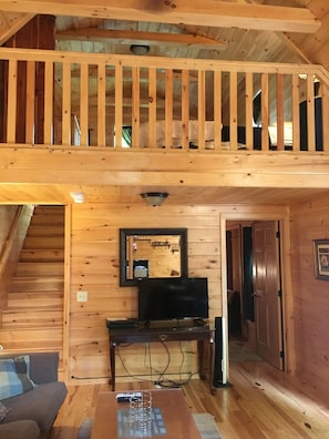 Un interior de madera con un entrepiso con dormitorio, un televisor y un comedor.