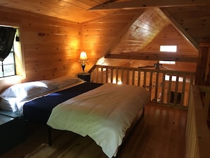 Un dormitorio acogedor en el ático con cama, mesita de noche, lámpara y ventana con cortinas.