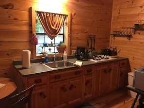 Cocina estilo cabaña de madera con un ventanal grande, un lavamanos, una cafetera y una encimera con varios objetos.