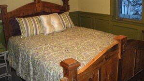 Uma cama com cabeceira de madeira e colcha estampada num quarto com paredes verdes e janela com vista para árvores.