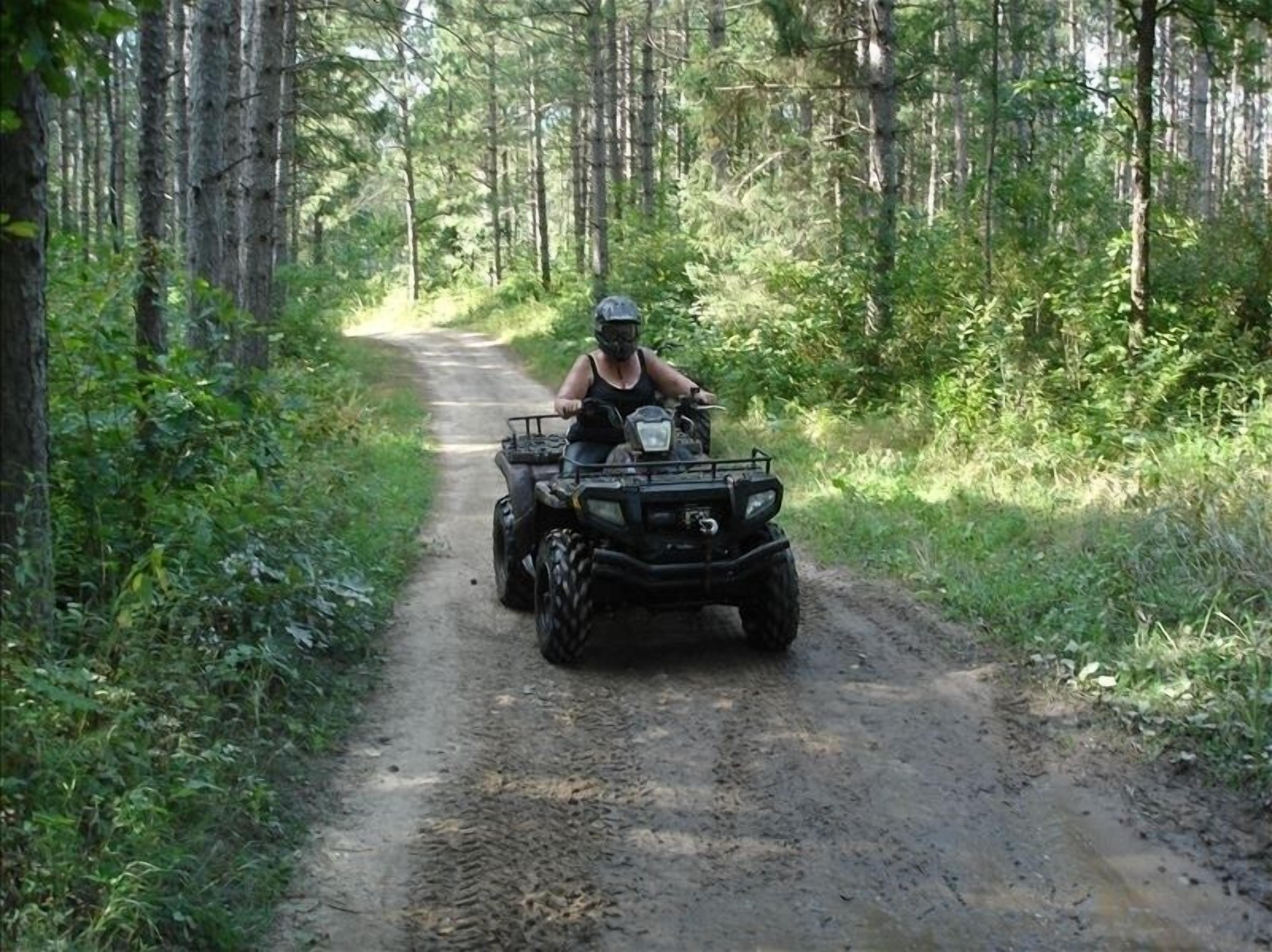 Iemand rijdt op een quad over een zandpad, omringd door dicht bos.