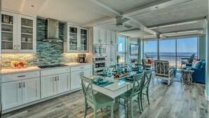Una cocina moderna con armarios blancos, una mesa de comedor de vidrio y vista al océano.