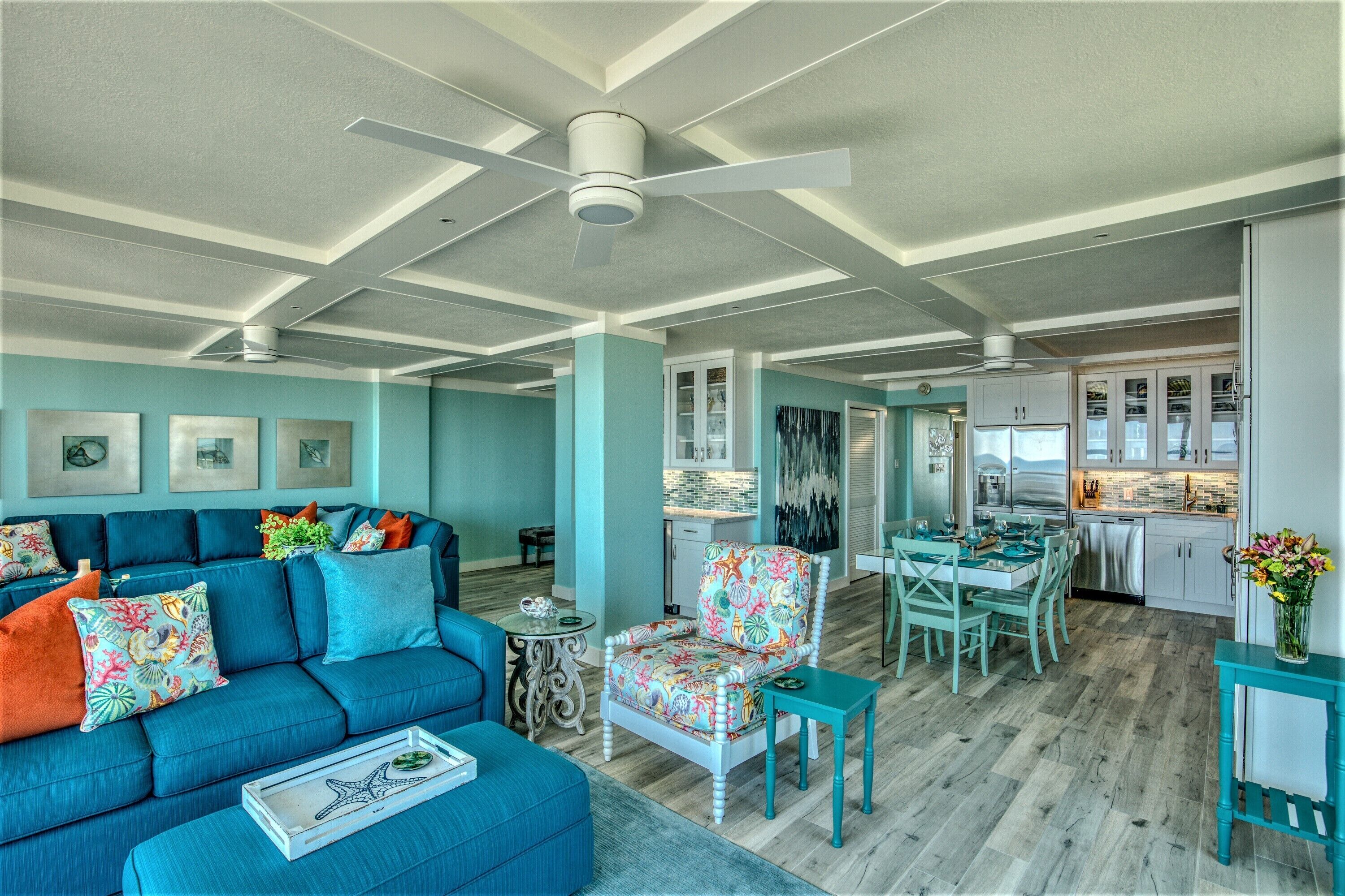 A spacious living room with a blue sofa, a dining area with a table and chairs, and a kitchen with cabinets and a countertop.