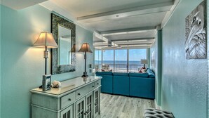 Una sala de estar moderna con un ventanal que da al océano, un sofá color turquesa y un mueble de madera con espejo.