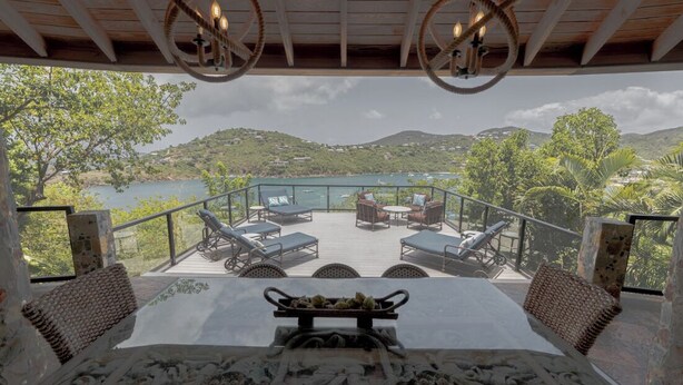 A terrace with a table, chairs, and a view of a lake and hills. - Updated Caribbean retreat, with solar and generator power backup (Cruz Bay)
