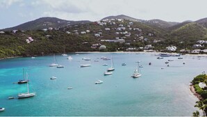 A coastal area with numerous boats anchored in clear turquoise waters, surrounded by lush green hills and residential buildings. - Updated Caribbean retreat, with solar and generator power backup (Cruz Bay)