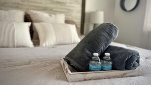 A neatly made bed with a wooden headboard, a tray with two bottles of water, and a rolled towel. - Eternal Summer 2-bedroom villa steps to Coligny Beach and Plaza (Hilton Head Island)