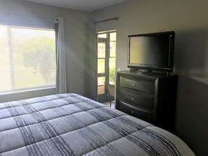 Relax in a cozy space with a neatly made bed and a TV on a dresser, offering a door to an outdoor area.