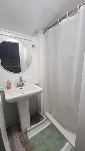 Un baño con un lavabo blanco, un espejo, una cortina de ducha y una alfombra verde a rayas.