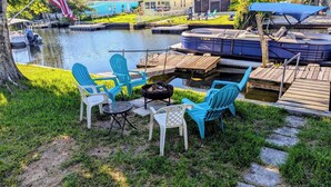 A deck with outdoor seating, a fire pit, and a view of a water body with boats. - Home on canal near Rogers Park, 2 docks, water access to the Gulf, sleeps 10 (Weeki Wachee)