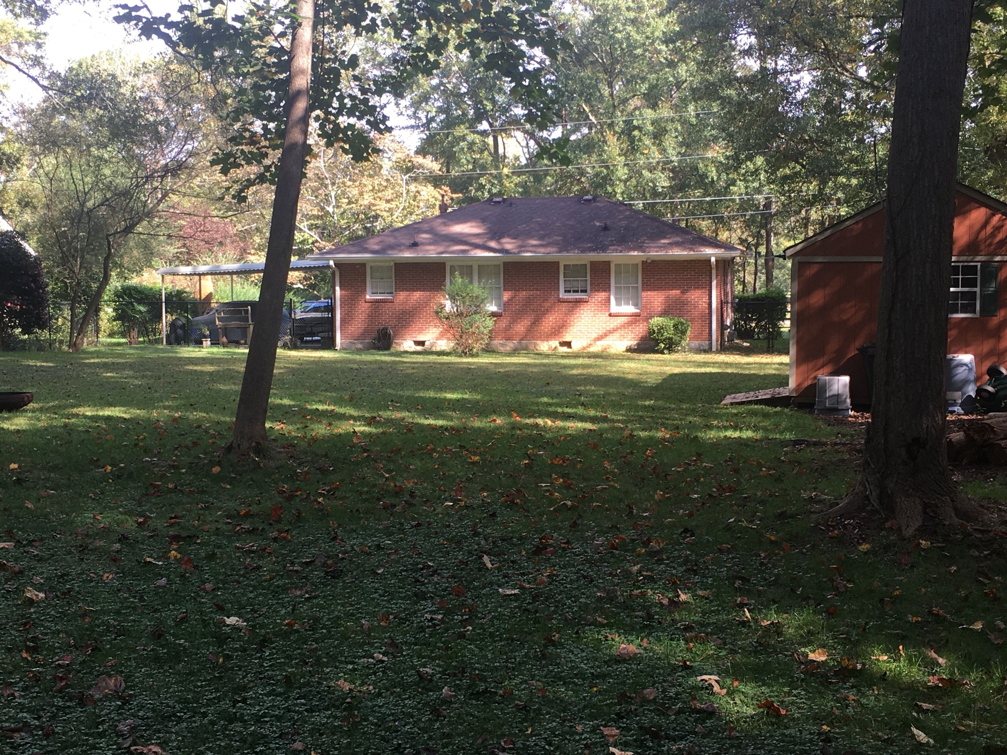 Il s’agit d’une propriété résidentielle comprenant une maison en briques, un petit abri de jardin et une pelouse parsemée de feuilles.
