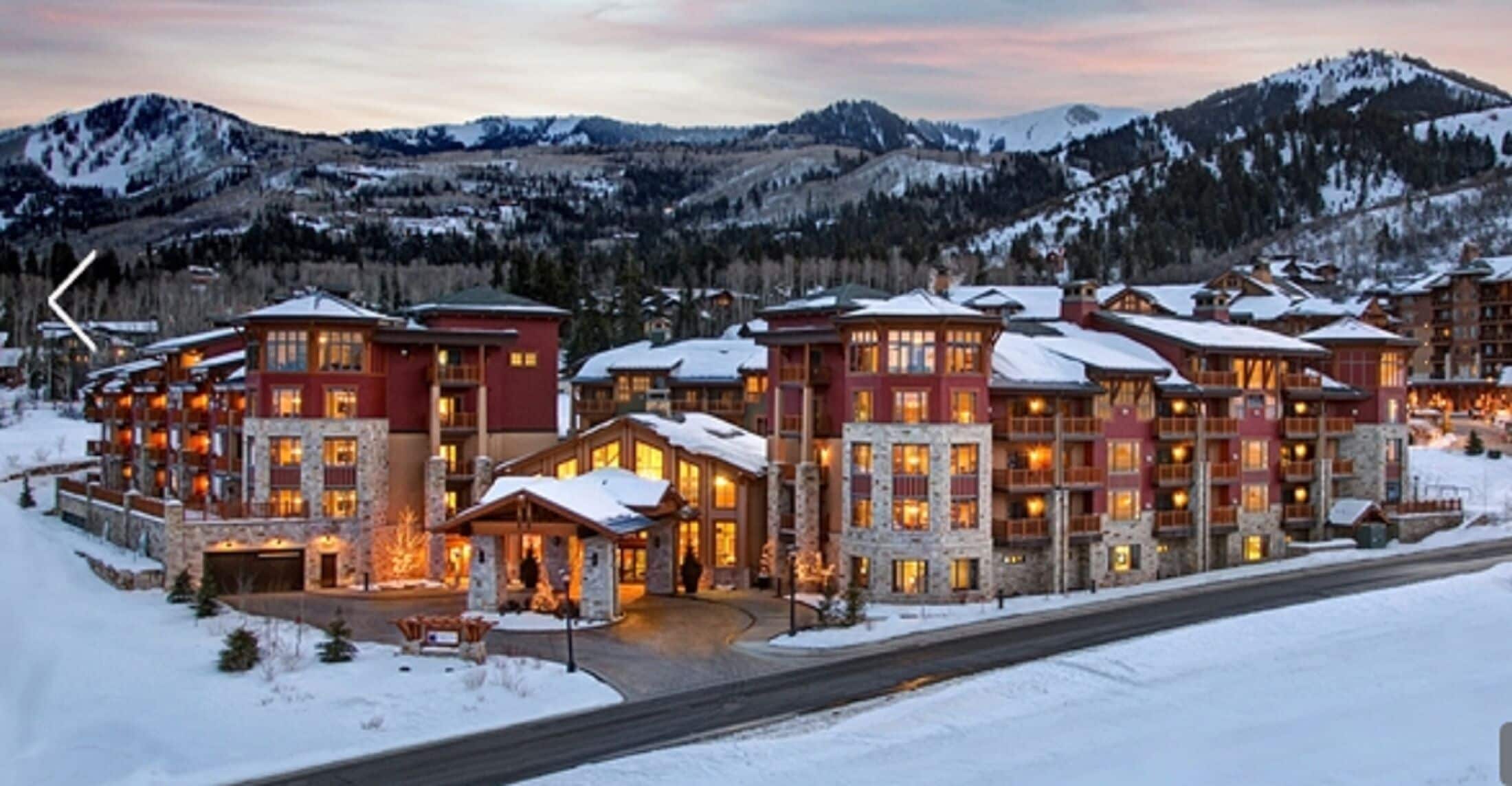 Un chalet à étages doté d’une façade en pierre, de grandes fenêtres et d’un toit recouvert de neige.