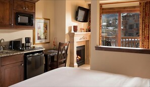 Quarto de hotel com cama, área de refeições com mesa e cadeiras, cozinha equipada com micro-ondas, cafeteira e lareira.