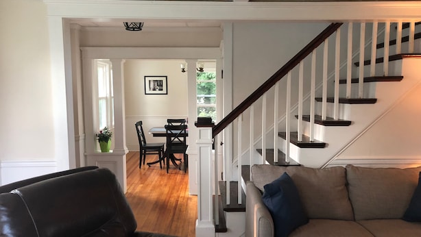 Ein Wohnzimmer mit Ledersessel, grauem Sofa und einer Treppe mit weißen Geländern.