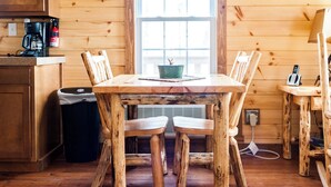 Une table à manger rustique en bois, accompagnée de quatre chaises, d’une machine à café et d’une poubelle, dans une pièce aménagée dans le style d’un chalet.