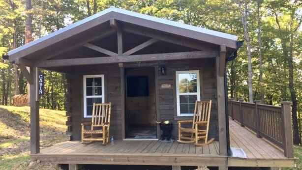 Une cabane avec une véranda, deux fauteuils à bascule et une pancarte indiquant « CABANE ».