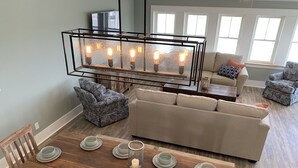 A dining area with a wooden table set for six, a sofa, and a modern pendant light fixture. - Steps to Beach*Private Heated Pool*Elevator* Jennette's Pier (Nags Head)