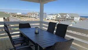 A covered outdoor dining area with a table and chairs, overlooking a residential area and the ocean. - Steps to Beach*Private Heated Pool*Elevator* Jennette's Pier (Nags Head)