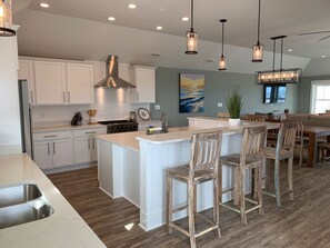 A modern kitchen with white cabinets, a large island with bar stools, and pendant lighting. - Steps to Beach*Private Heated Pool*Elevator* Jennette's Pier (Nags Head)