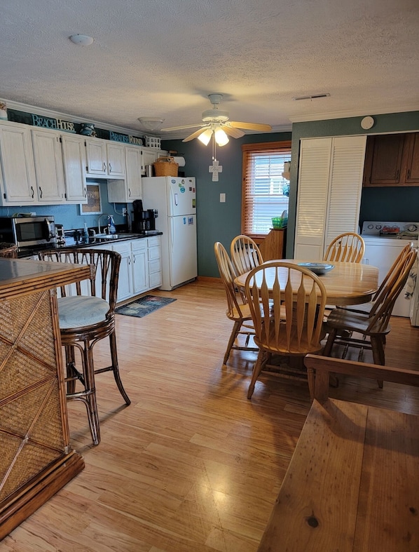 A kitchen with white cabinets, a dining table with chairs, and a ceiling fan.