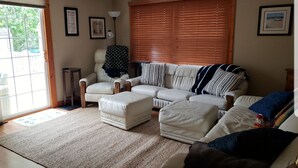 A living room with a beige sofa, a white armchair, and a coffee table. There is a window with blinds, a lamp, and framed pictures on the wall. - Relaxing Gem Beach, Close to Twin Oast Brewery, Orchard Eatery and Miller Ferry (Port Clinton)