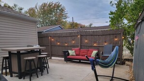 A backyard with a wooden fence, a red sofa, a hammock, a dining table with stools, and string lights. - Relaxing Gem Beach, Close to Twin Oast Brewery, Orchard Eatery and Miller Ferry (Port Clinton)