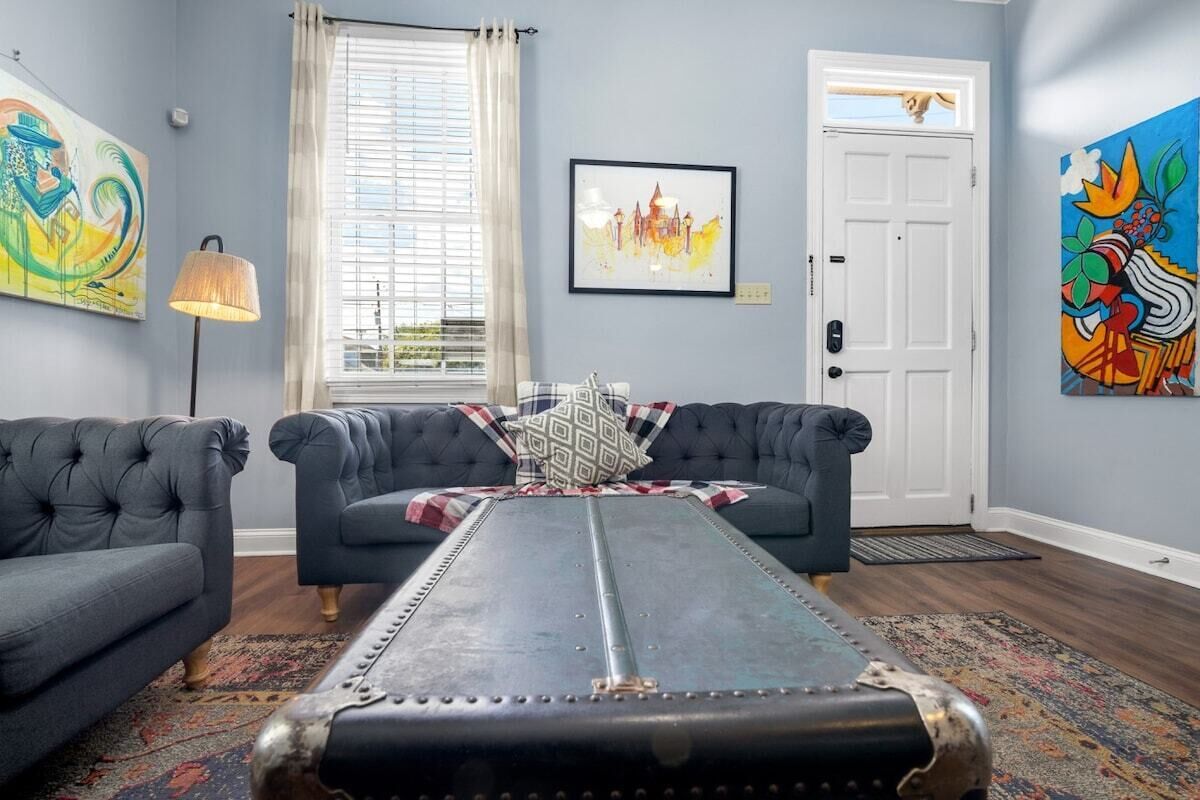 Een woonkamer met twee donkere banken, een kamerkleed met patroon, een metalen tafel en kunstwerken aan de muur.