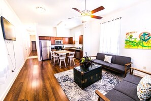 Relax in a cozy living space with a sofa, coffee table, and rug. Enjoy meals in the adjacent dining area with white chairs.