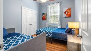 Ein Schlafzimmer mit zwei Betten, einem Deckenventilator, einem Fenster mit Jalousien und einem Gemälde an der Wand.