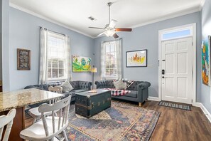 Een woonkamer met een eettafel, twee banken, een plafondventilator en kunstwerken aan de wanden.