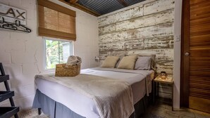 Un dormitorio con cama, mesita de noche, pared de madera, ventana y puerta.