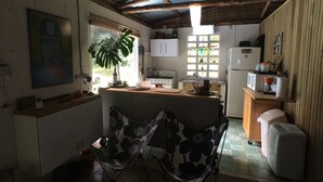 A compact kitchen with a wooden counter, a refrigerator, a microwave, and a stove. There is a chair with a floral pattern and a potted plant. - CHARMING  FOREST LOG CABIN (utuado)