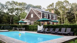 Une terrasse en bois avec une piscine, des chaises longues et des parasols.