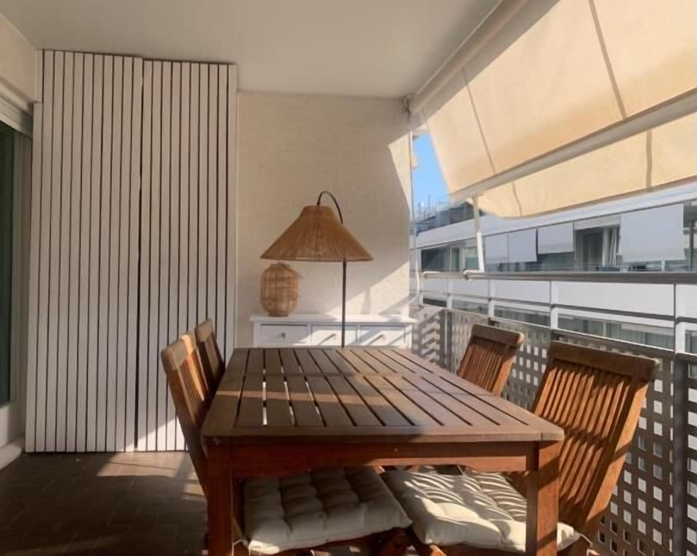 A balcony with a wooden table and chairs, a woven lamp, and a view of a building.