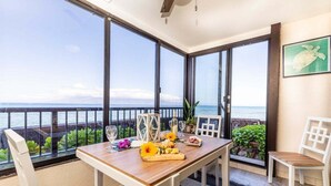 Un balcon avec une table en bois dressée pour le dîner, une chaise blanche et une vue sur l’océan.