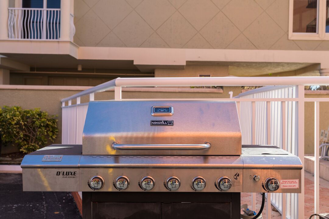 Un barbecue à gaz D'Luxe doté de plusieurs brûleurs et d’un écran numérique, installé à l’extérieur, devant un immeuble avec balcon.