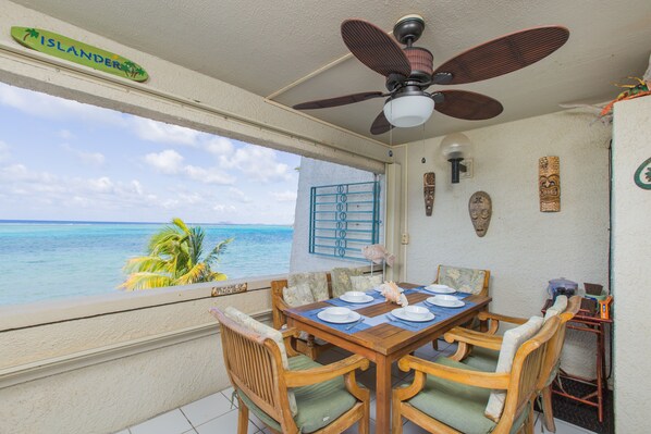 Un comedor con vista al océano, un ventilador de techo y decoración de pared tropical.