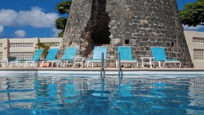 Ein Swimmingpool mit blauen Stühlen und einem dahinter liegenden Stein-Turm.