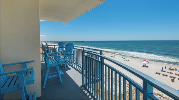 A balcony with blue chairs and a view of the beach.