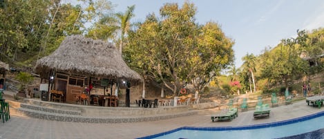 A pool area with a thatched-roof structure, lounge chairs, and a dining area.