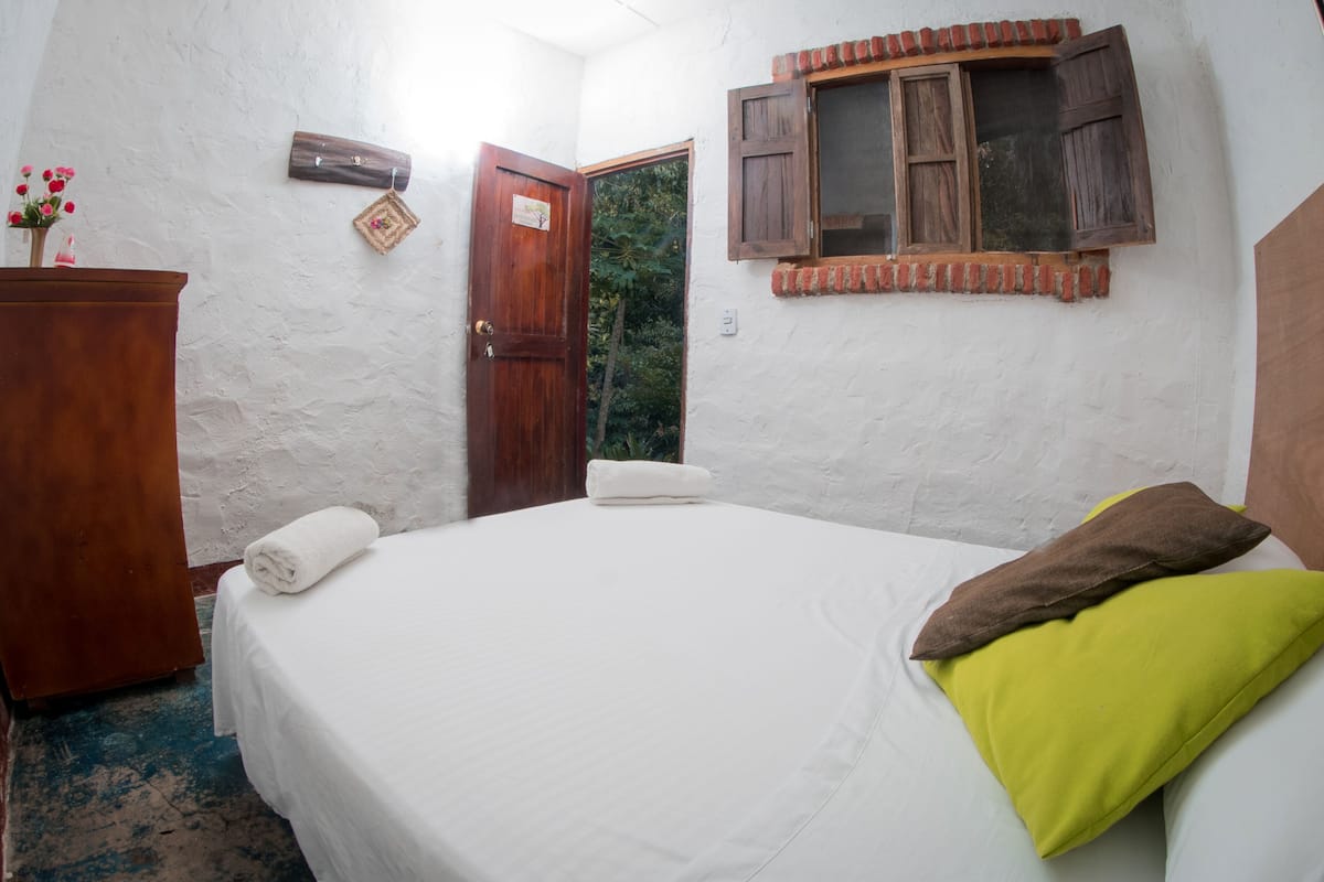 A bedroom with a bed, a wooden wardrobe, a door, and a window with shutters.