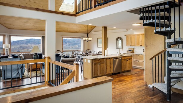 A spacious living area with a wooden staircase, a kitchen with wooden cabinets, and a view of the mountains. - An Easy 3-Minute Walk to the Slopes! (Steamboat Springs)